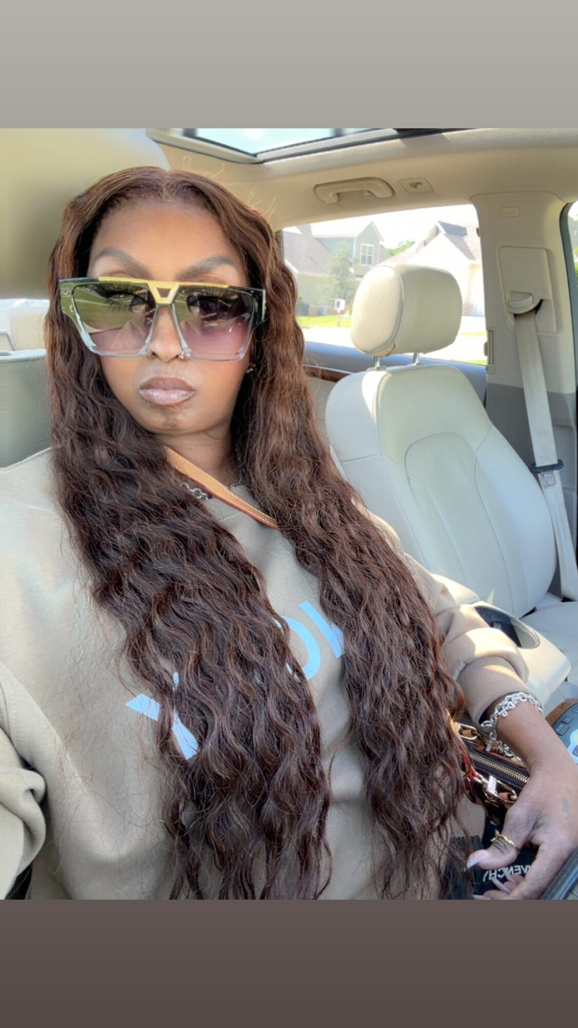 Woman with long wavy hair wearing sunglasses sitting in a car, sunlight visible through window.