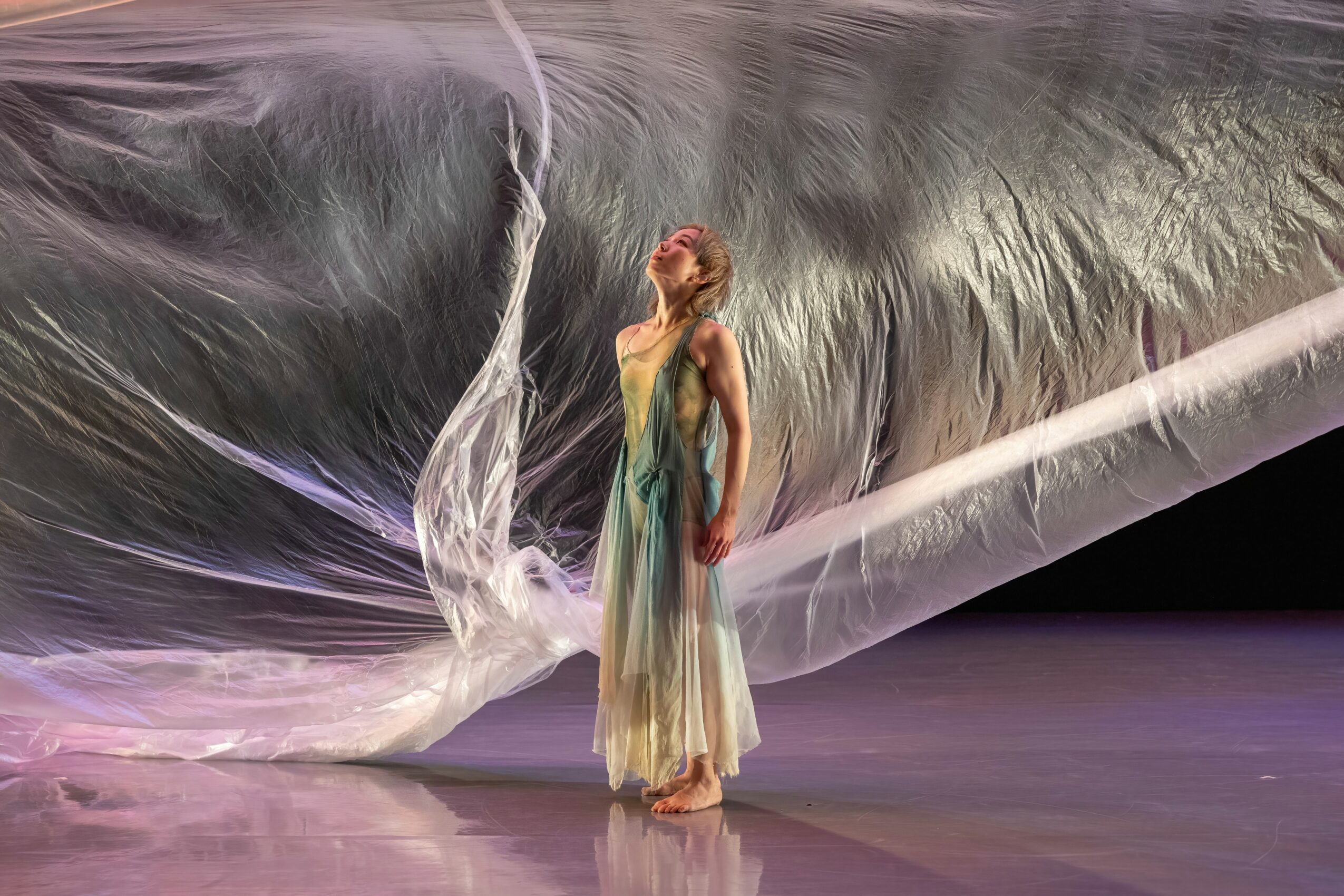 A woman in a flowing dress stands on stage with a large, translucent fabric backdrop behind her.