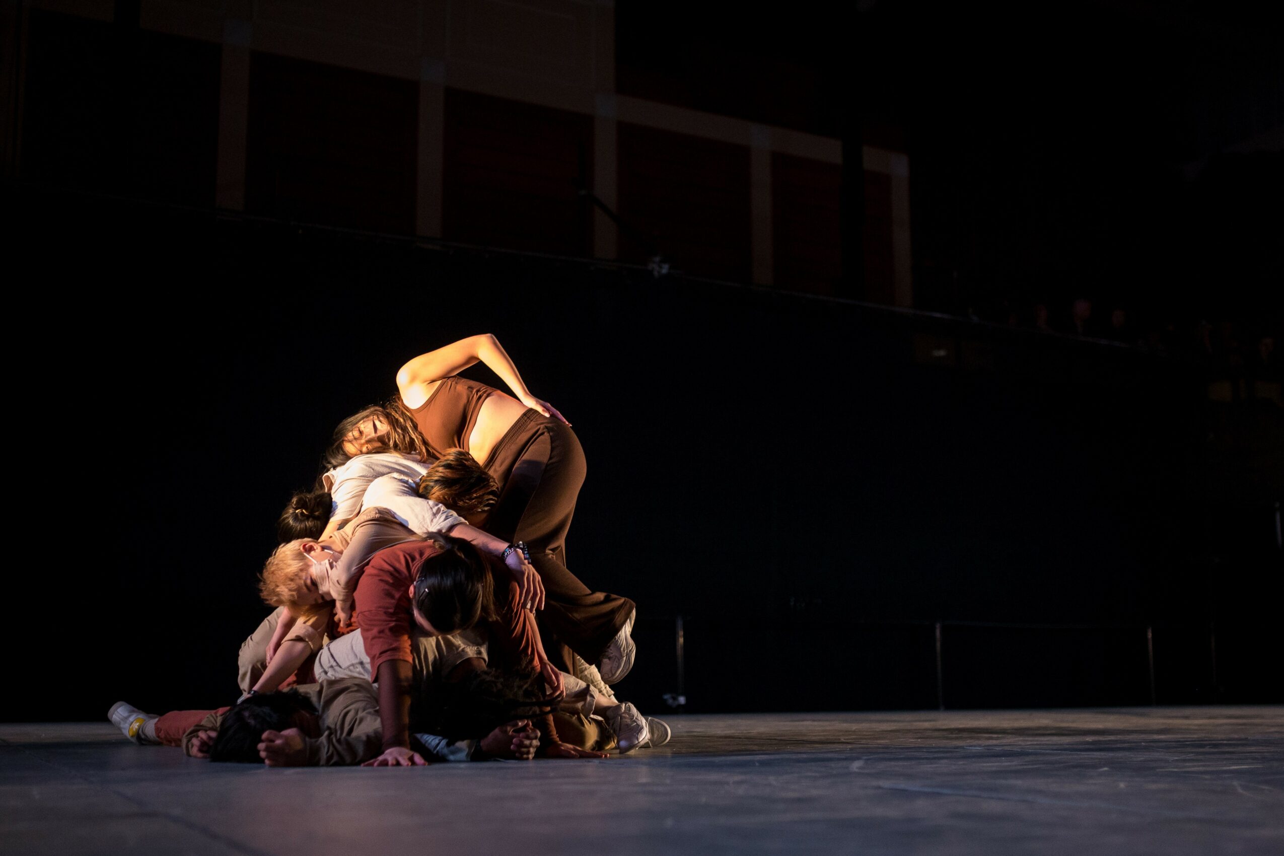Group of people performing a dance or theatrical act on stage, with some lying on the floor and others leaning over them.