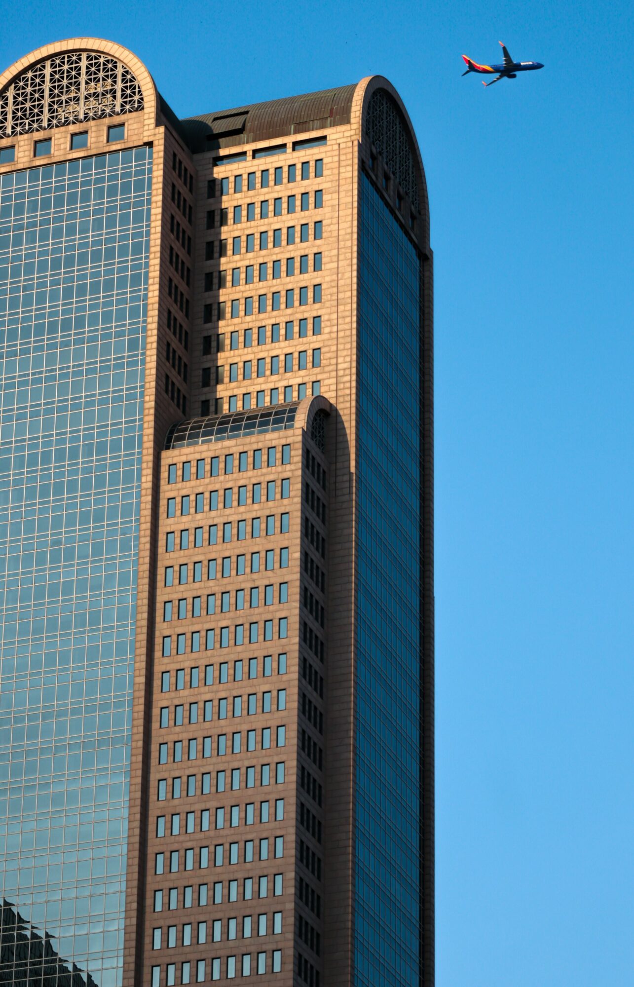 Tall modern building with a blue sky and airplane flying above, featuring curved architectural elements.