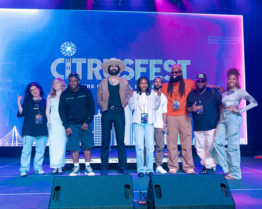 Group of nine people standing on stage in front of a large screen with 'CITROFEST' text, smiling and posing for photo.