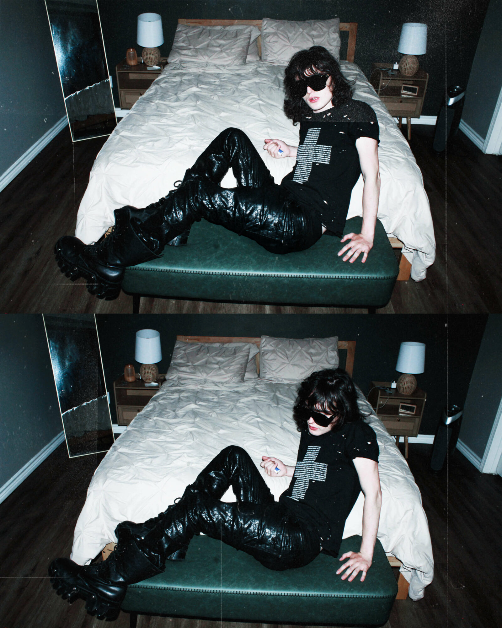 Person with dark curly hair, sunglasses, black outfit, and shiny pants sitting on a bed in a bedroom, with two nightstands and lamps.