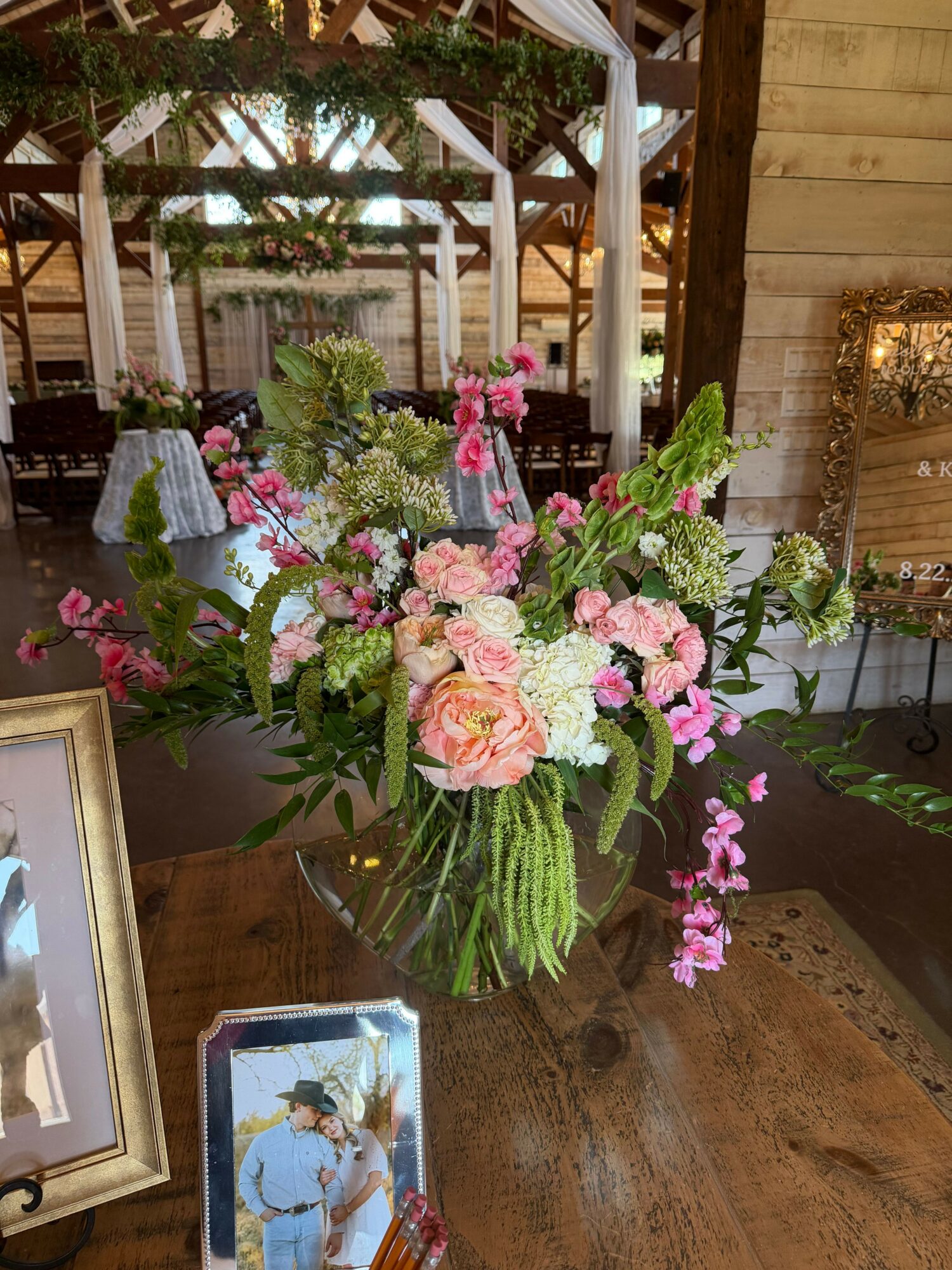 Colorful flower arrangement with pink, white, and green flowers on a wooden table, with a framed photo nearby.
