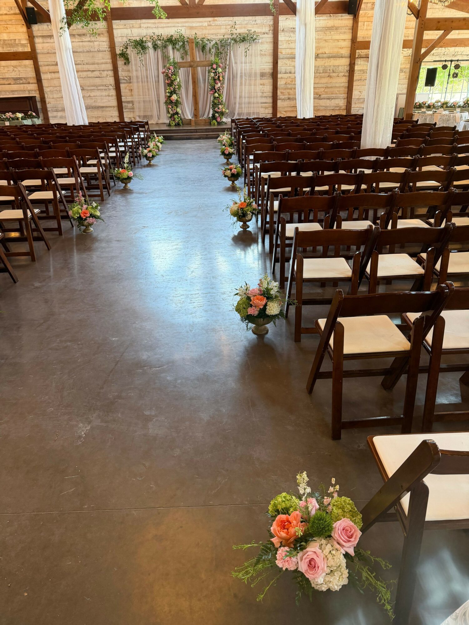 Indoor event space with rows of chairs and floral arrangements along the aisle, viewed from the side.