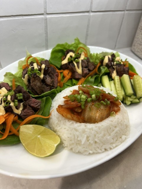 Plate with rice, grilled fish, fresh vegetables, and lemon wedge, set against a tiled wall background.