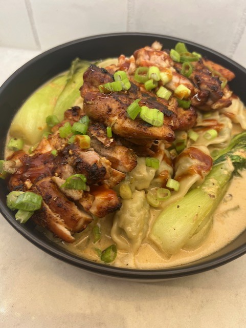 Bowl of grilled meat with green onions on top, served with lettuce and creamy sauce, in a black bowl.