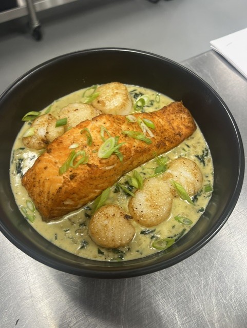 Bowl with fried fish fillet, round potato balls, and green onion in creamy sauce.