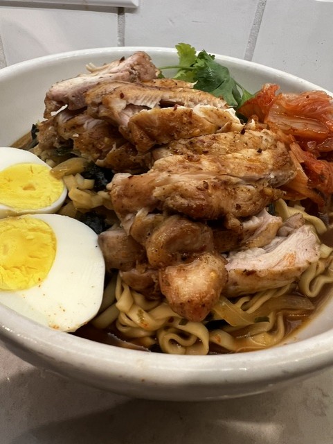 Bowl of noodles with chicken, boiled egg halves, tomato, and cilantro garnish.