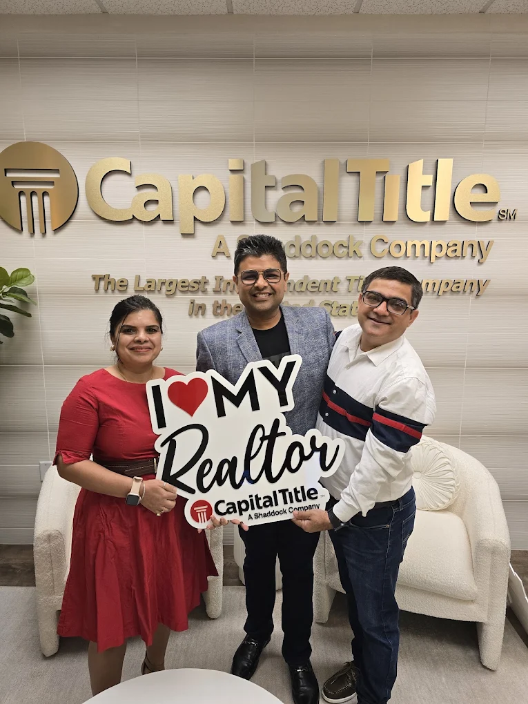 Three people holding a sign in front of a company sign, smiling, in an office setting.