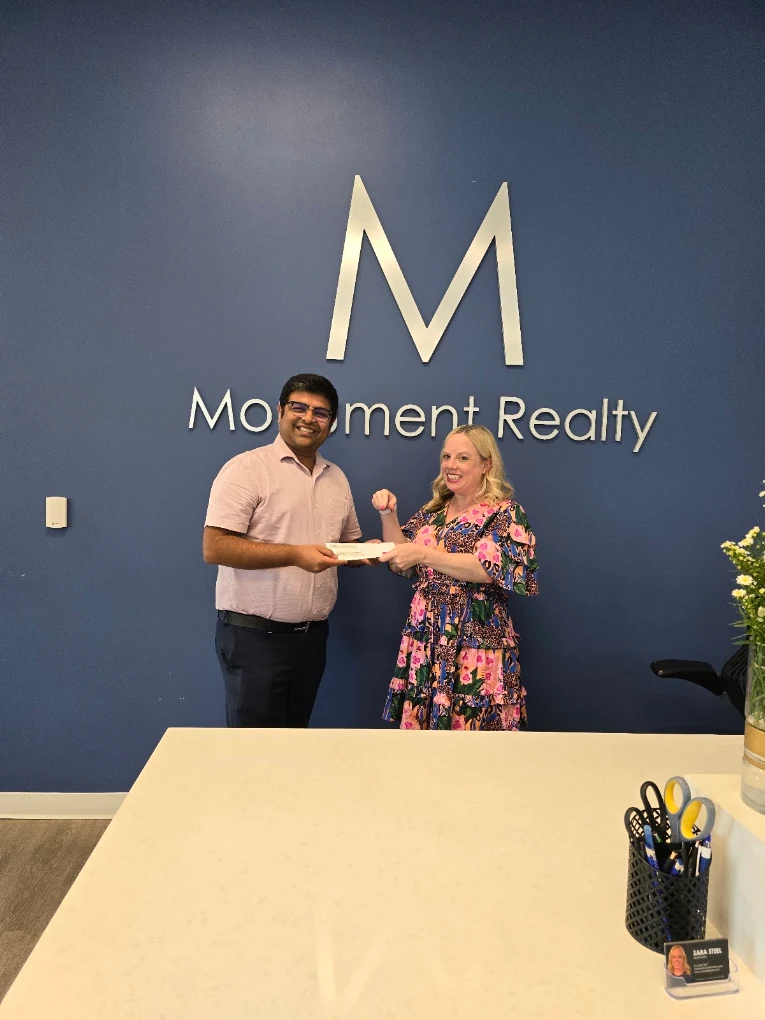 Two people shaking hands in front of a blue wall with a large letter 'M' and the words 'Movement Realty'.