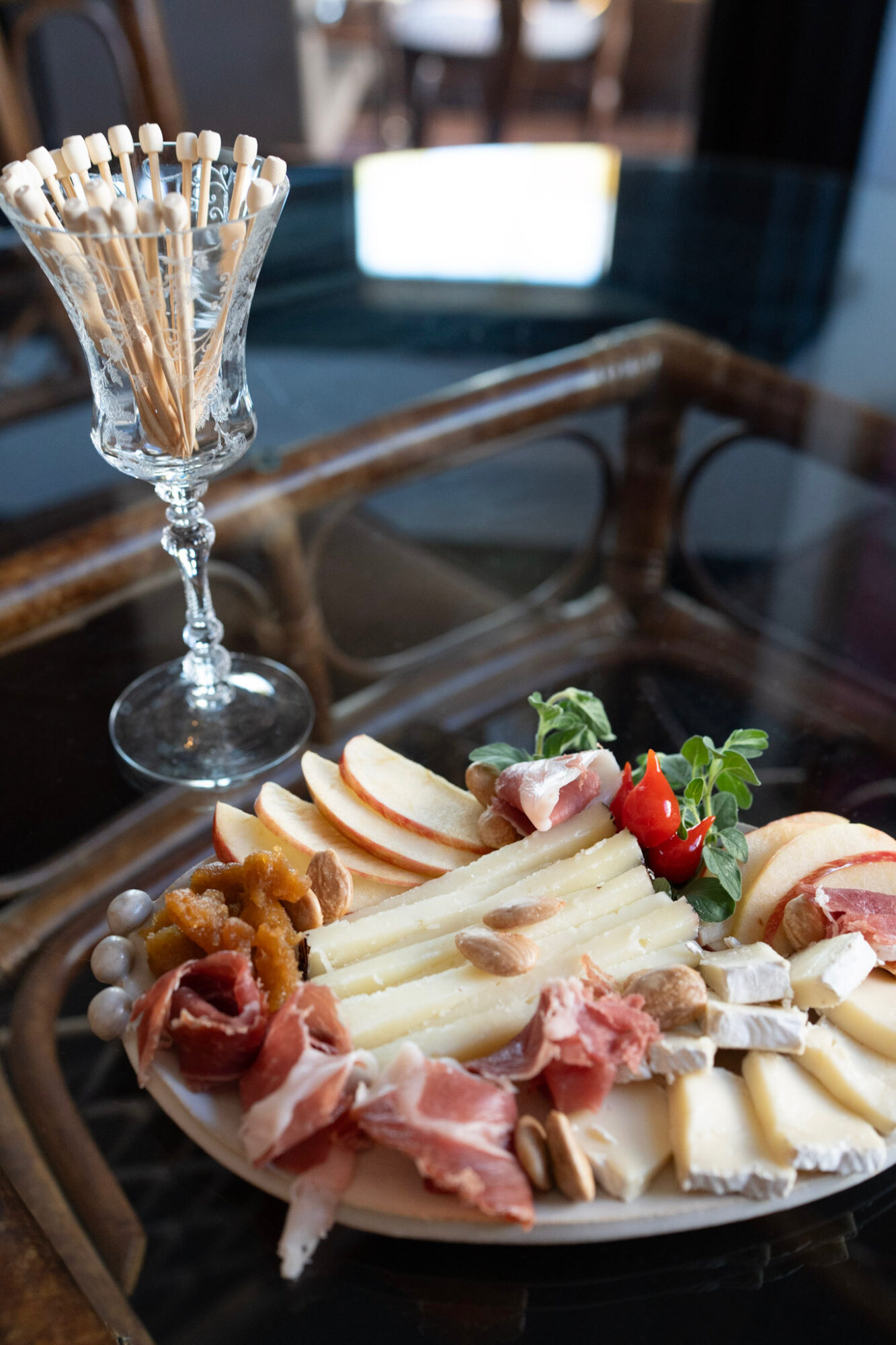 A glass container with toothpicks and a cheese and meat platter with strawberries and greens on a glass table.