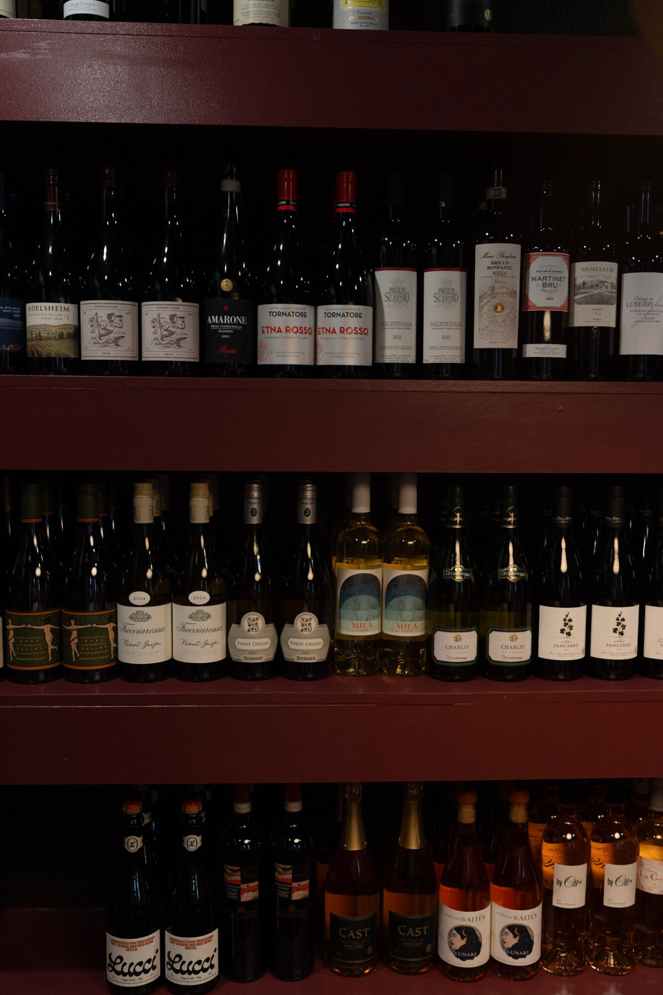 Shelf with bottles of wine and spirits arranged in rows, labels visible, dark background.