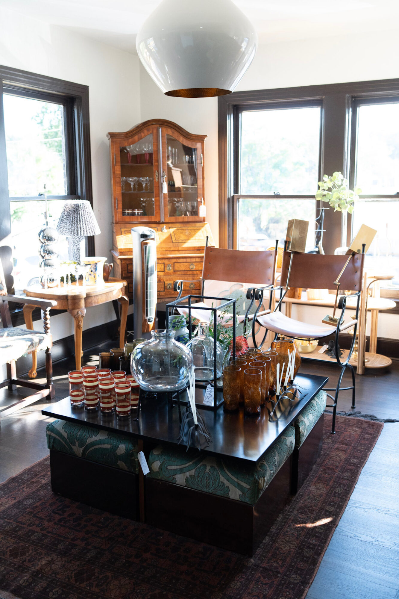 Living room with wooden furniture, large windows, and a dark coffee table with decorative items, rug, and a white pendant light.