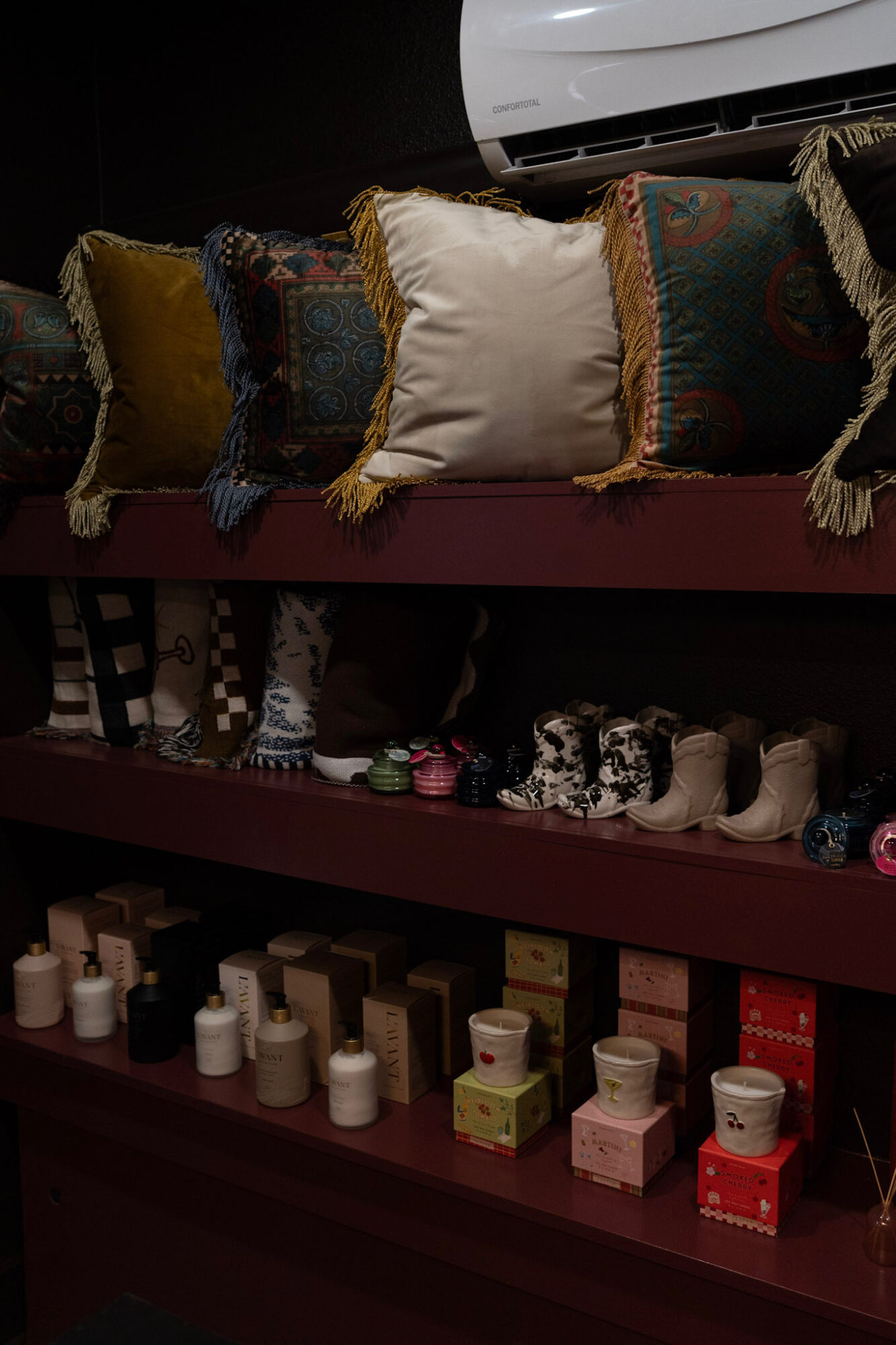 Shelf with decorative pillows on top and small bottles and boxes below, in a store setting.