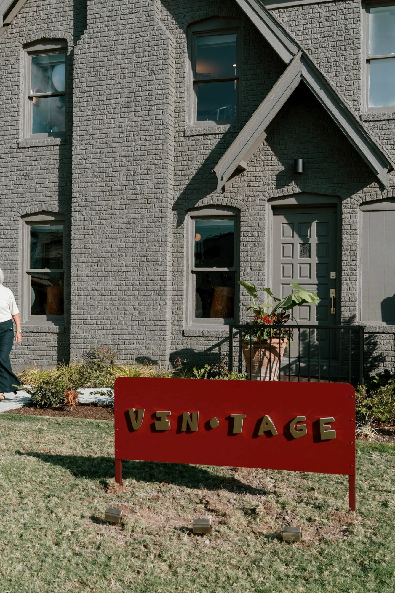 Front view of a gray brick house with a porch, windows, and a red sign reading 'VINTAGE' in front yard.