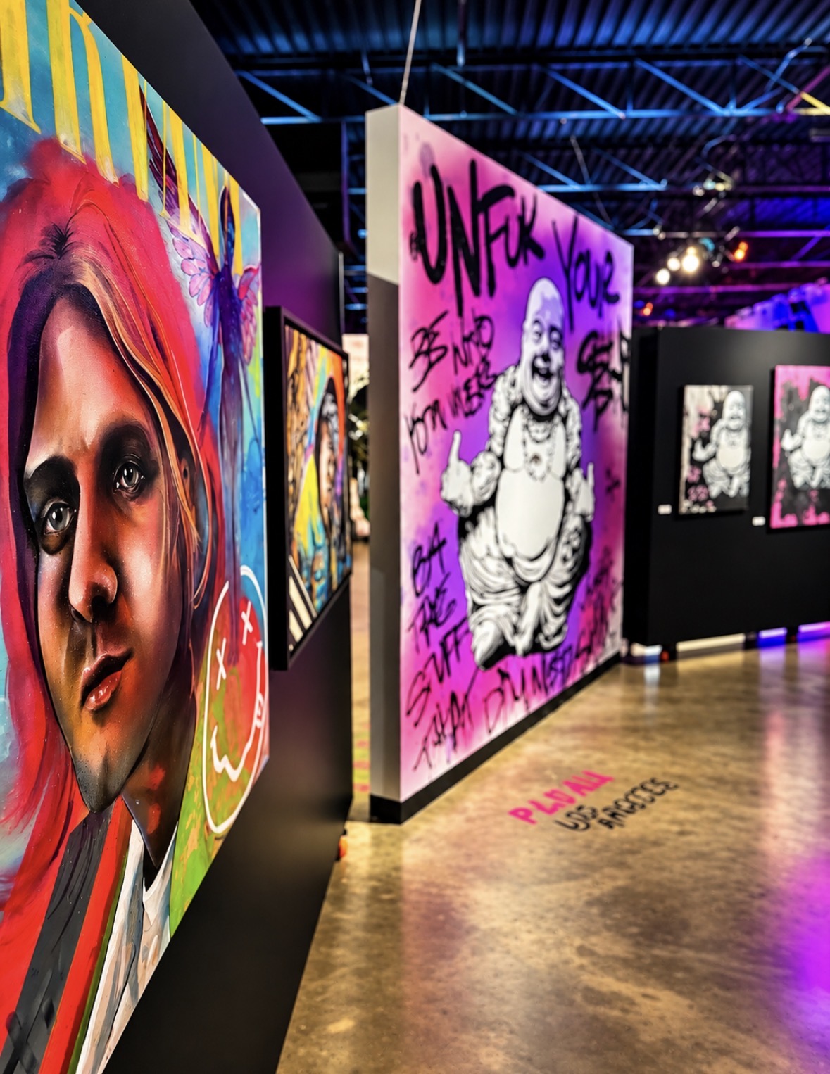 Art gallery with colorful portraits and graffiti-style artwork on walls, wooden floor, and black display panels.