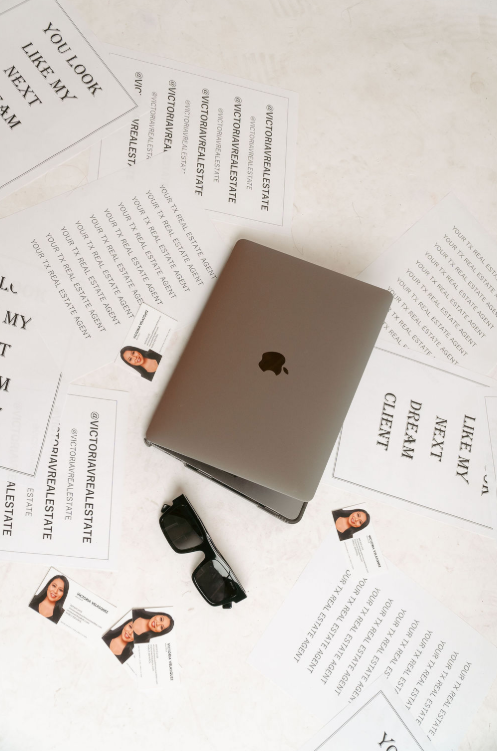 Closed laptop, sunglasses, and scattered papers with text and images on a white surface.