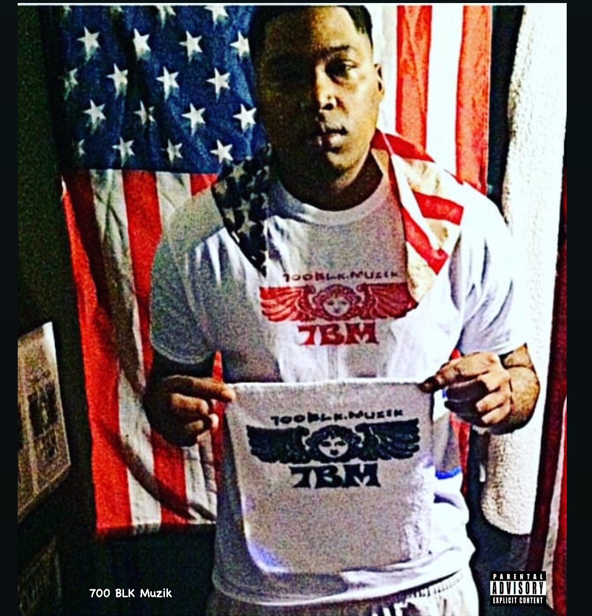 Person holding a T-shirt in front of an American flag, wearing a white shirt with red and black design, dark background