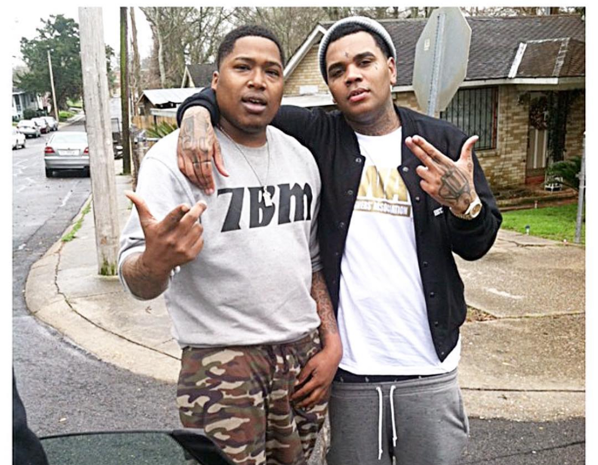 Two young men standing outdoors, one with arm around the other, making hand gestures, in a neighborhood setting.