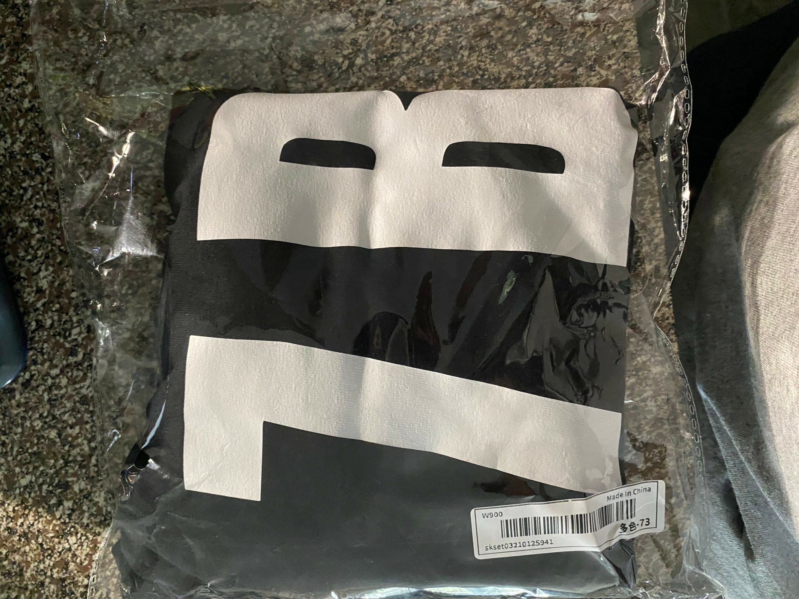 A black and white face mask with cutouts for eyes, packaged in clear plastic, placed on a dark surface.
