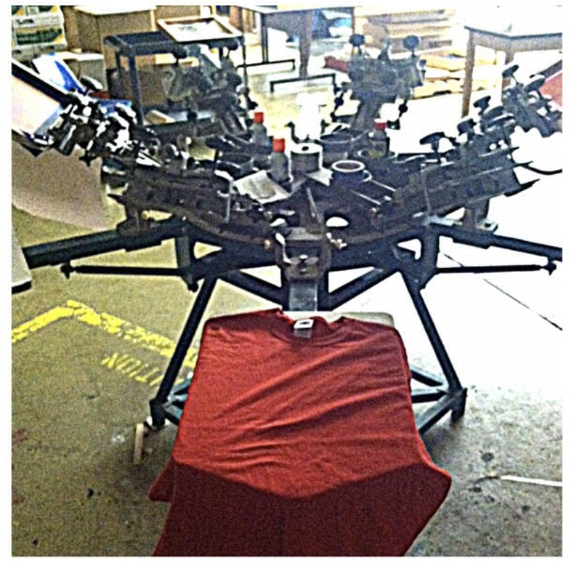 A drone with multiple cameras and equipment is displayed indoors, with a red cloth-covered object in front. Bright windows in background.