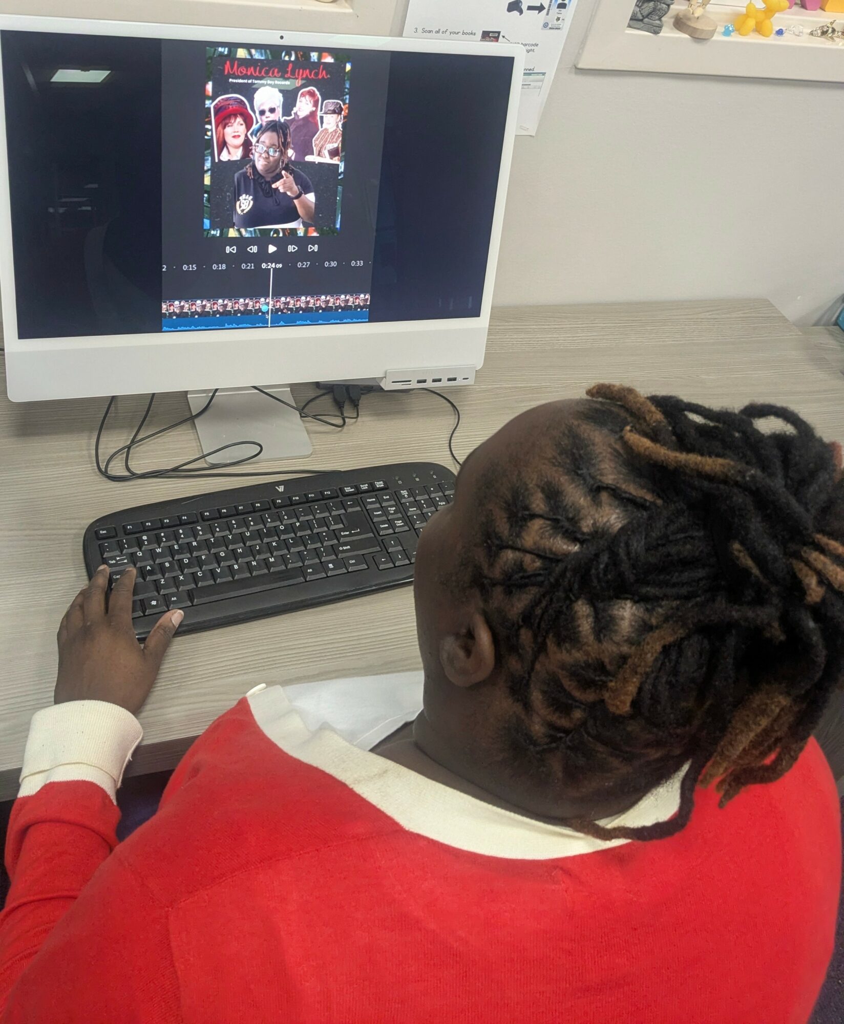 Child with braided hair in red and white clothing using a computer with a black keyboard, viewing a photo editing program.