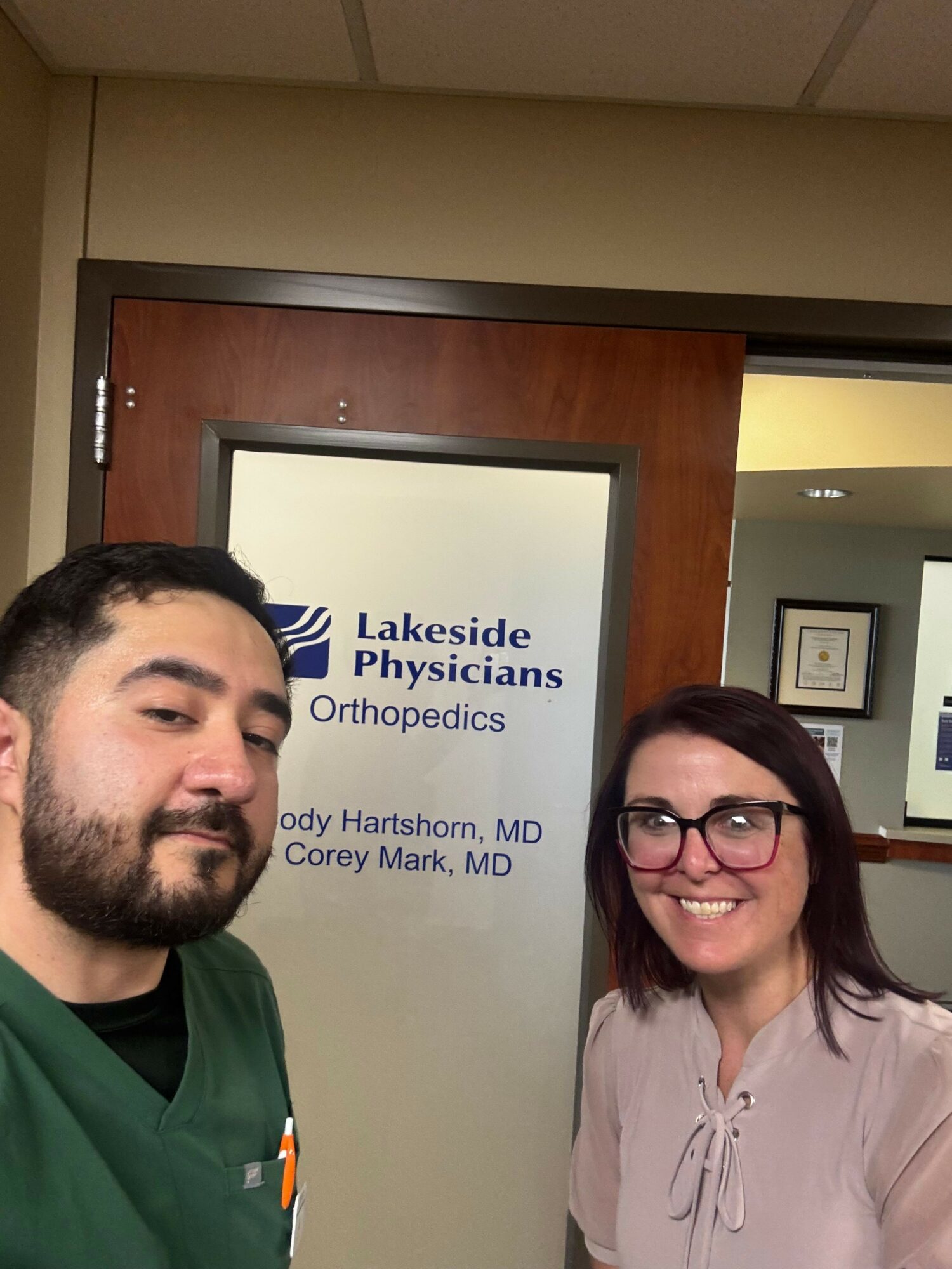 Two medical professionals, a woman and a man, standing in front of a sign for Lakeside Physicians, smiling.