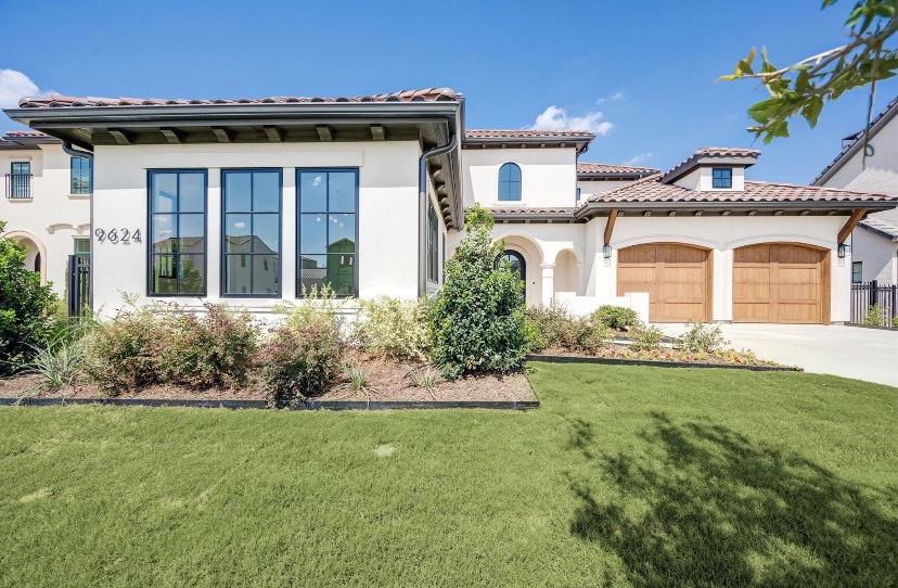 Modern house with large windows, a garage with wooden doors, and a well-maintained lawn and garden under a blue sky.