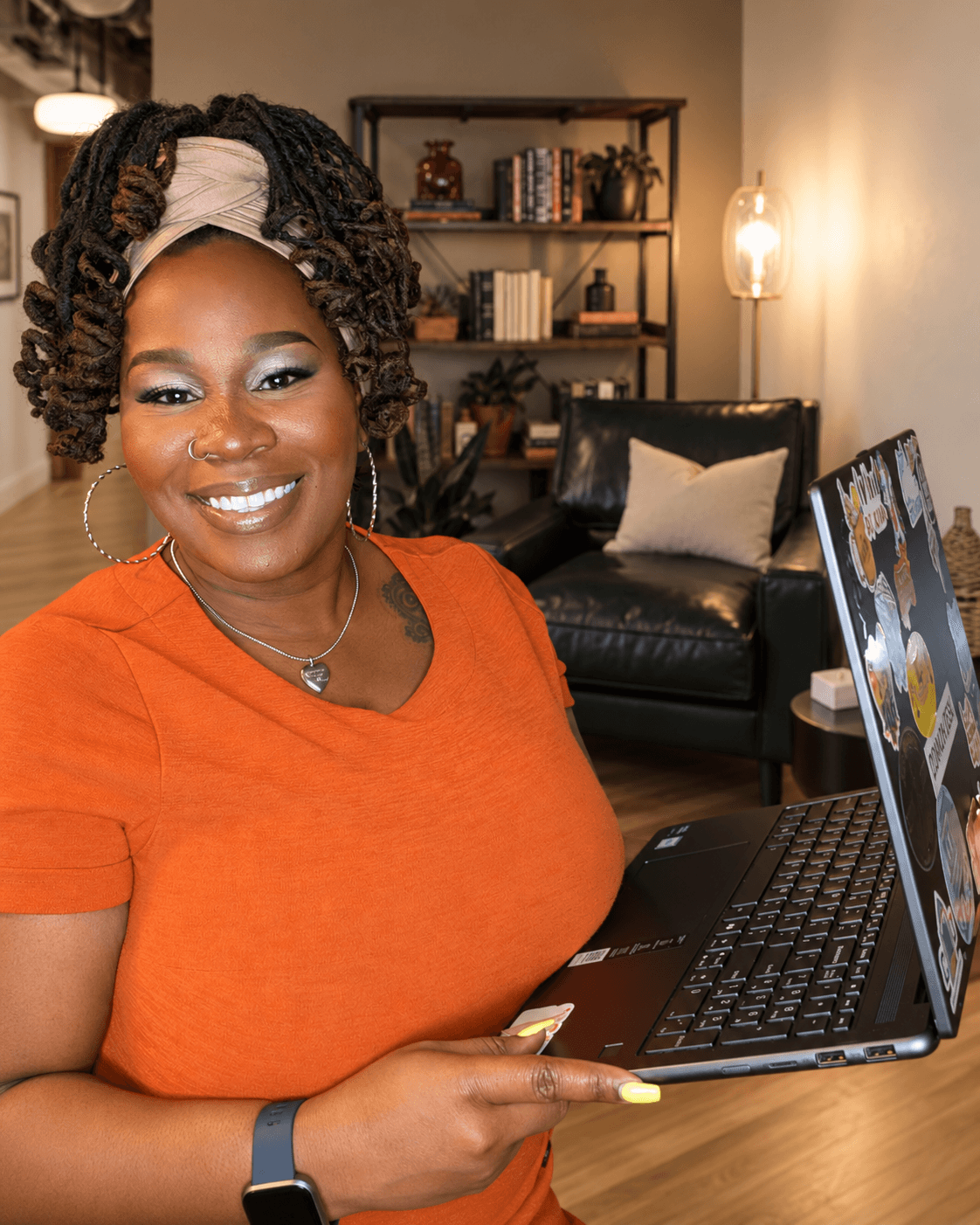 Smiling woman with curly hair and headband using a laptop in a cozy living room.
