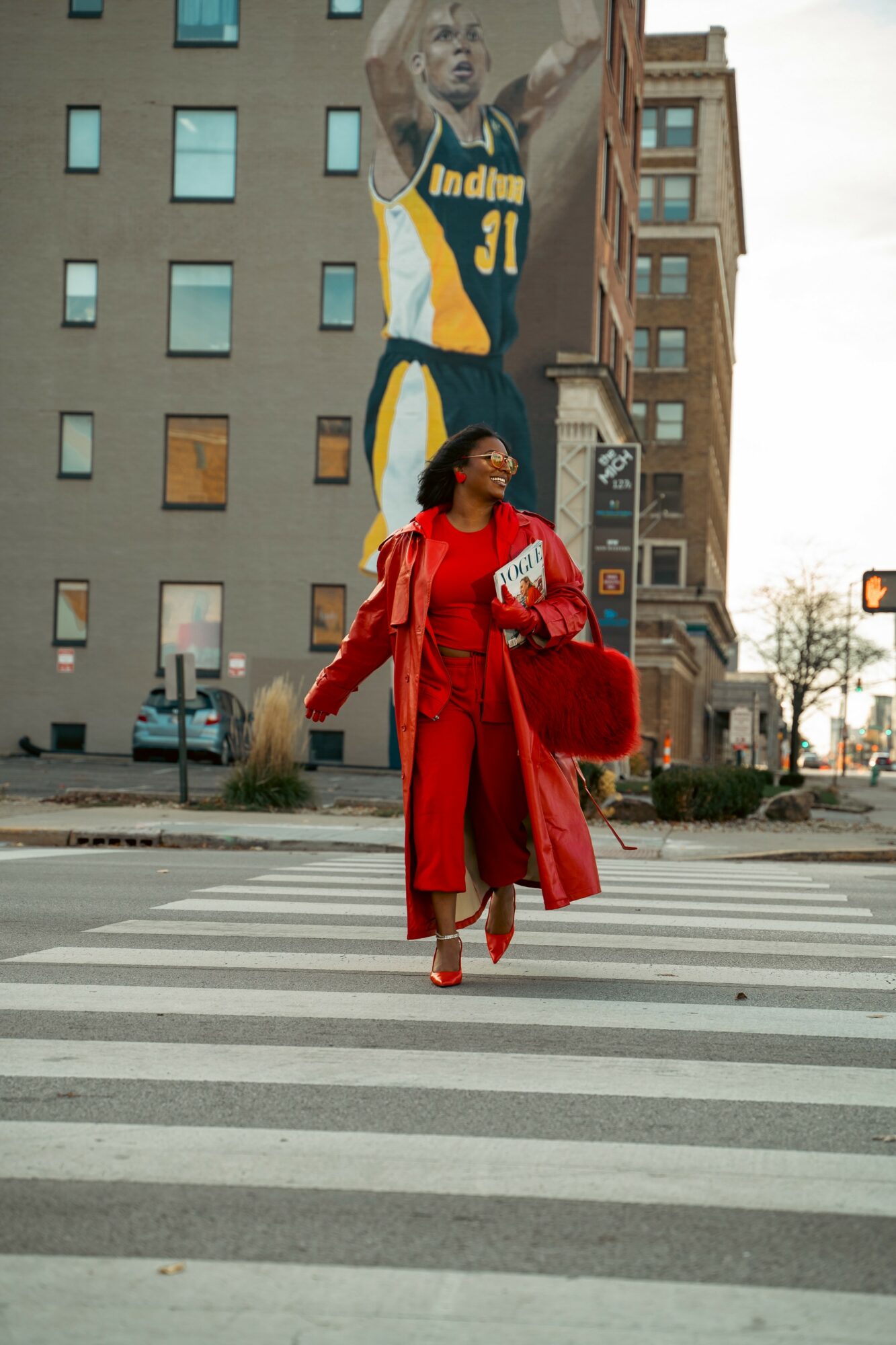 Woman in red coat crossing street with large mural of basketball player on building behind her.