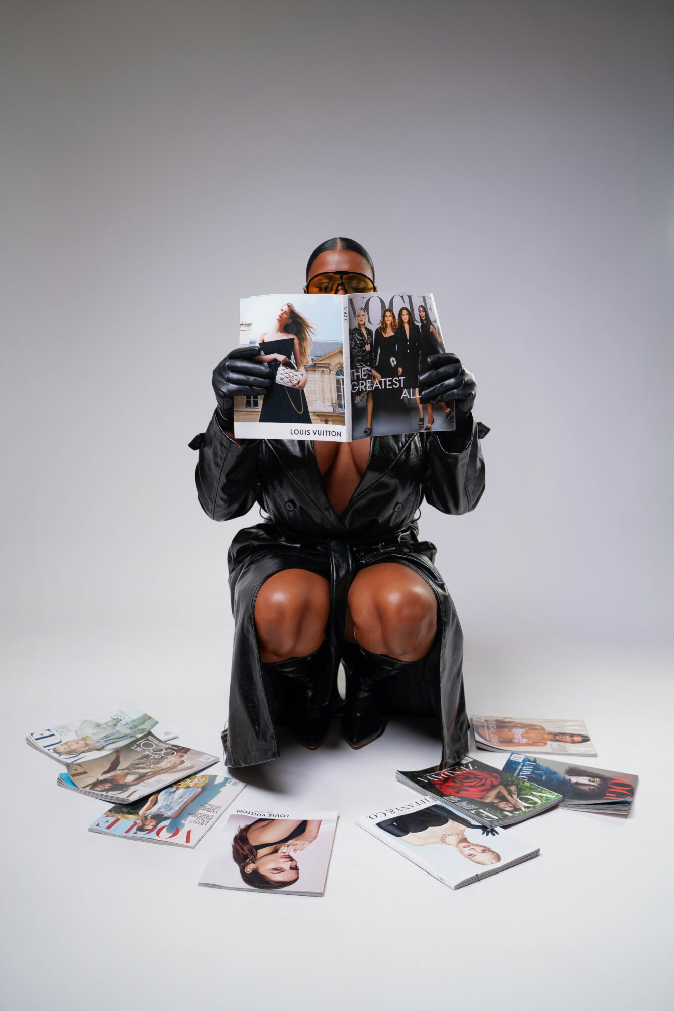 Person sitting on the floor reading a magazine, surrounded by scattered magazines, against a plain background.