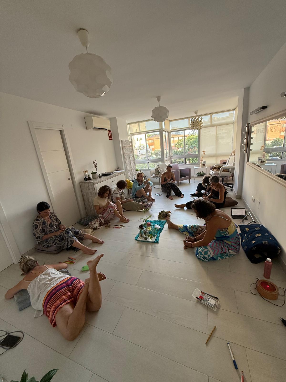 Group of children sitting and lying on the floor in a bright room with large windows, playing with toys and objects.