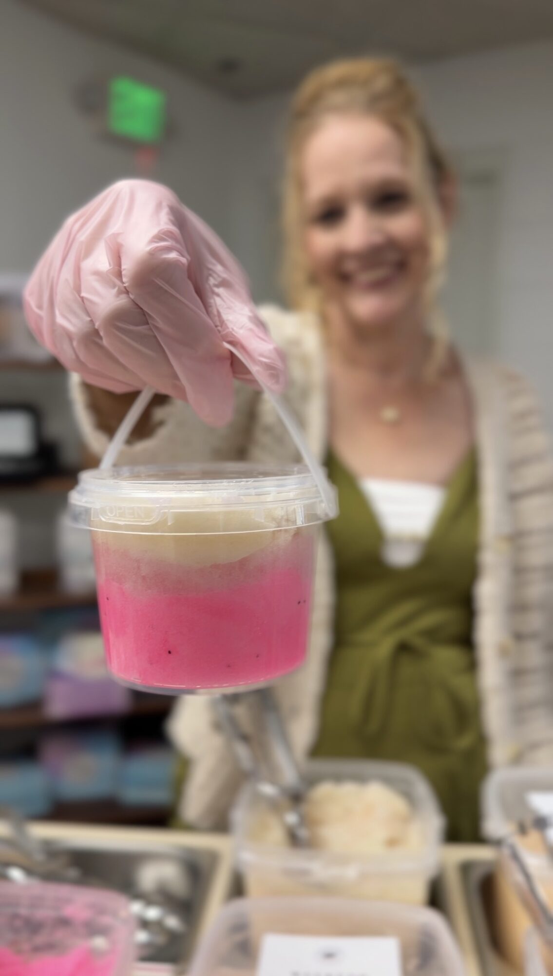 Person smiling in background with a pink and clear container with a pink object in foreground.