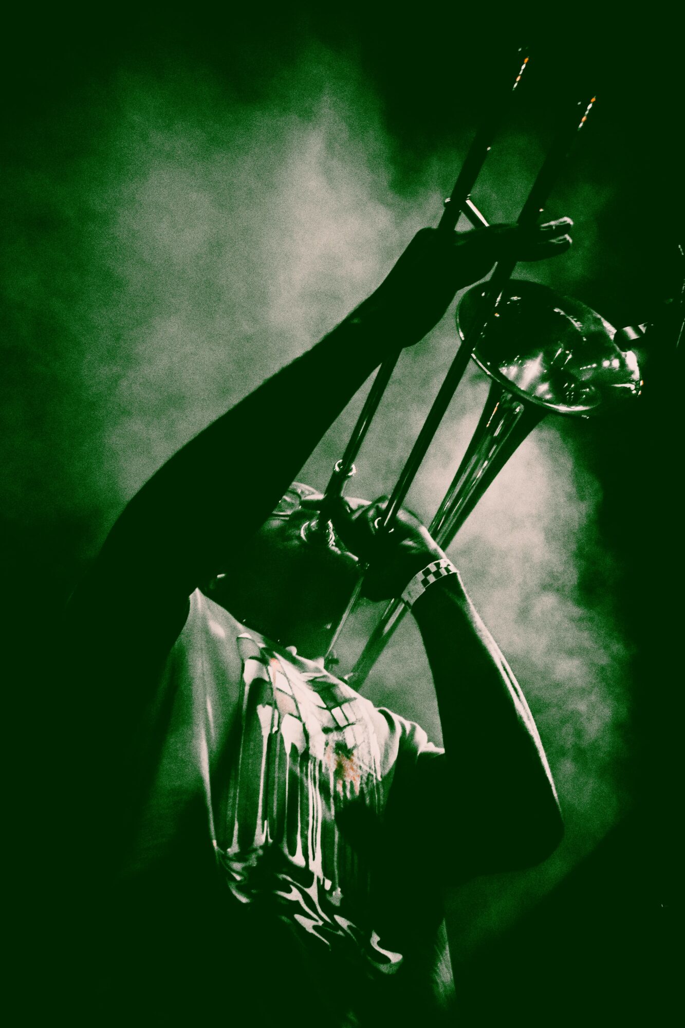 Person playing trumpet with smoke or fog in background, in a green-tinted image.