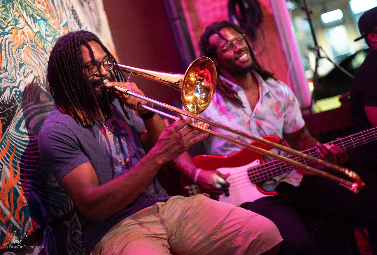 Two people playing musical instruments, one with a trombone and the other with a guitar, in a colorful setting.