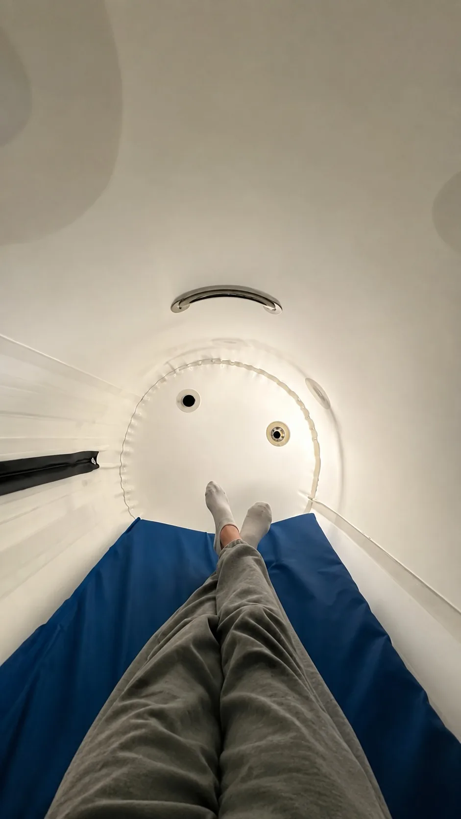 Person standing inside a circular tube, viewed from above, with legs and feet visible, wearing gray pants and white shoes.