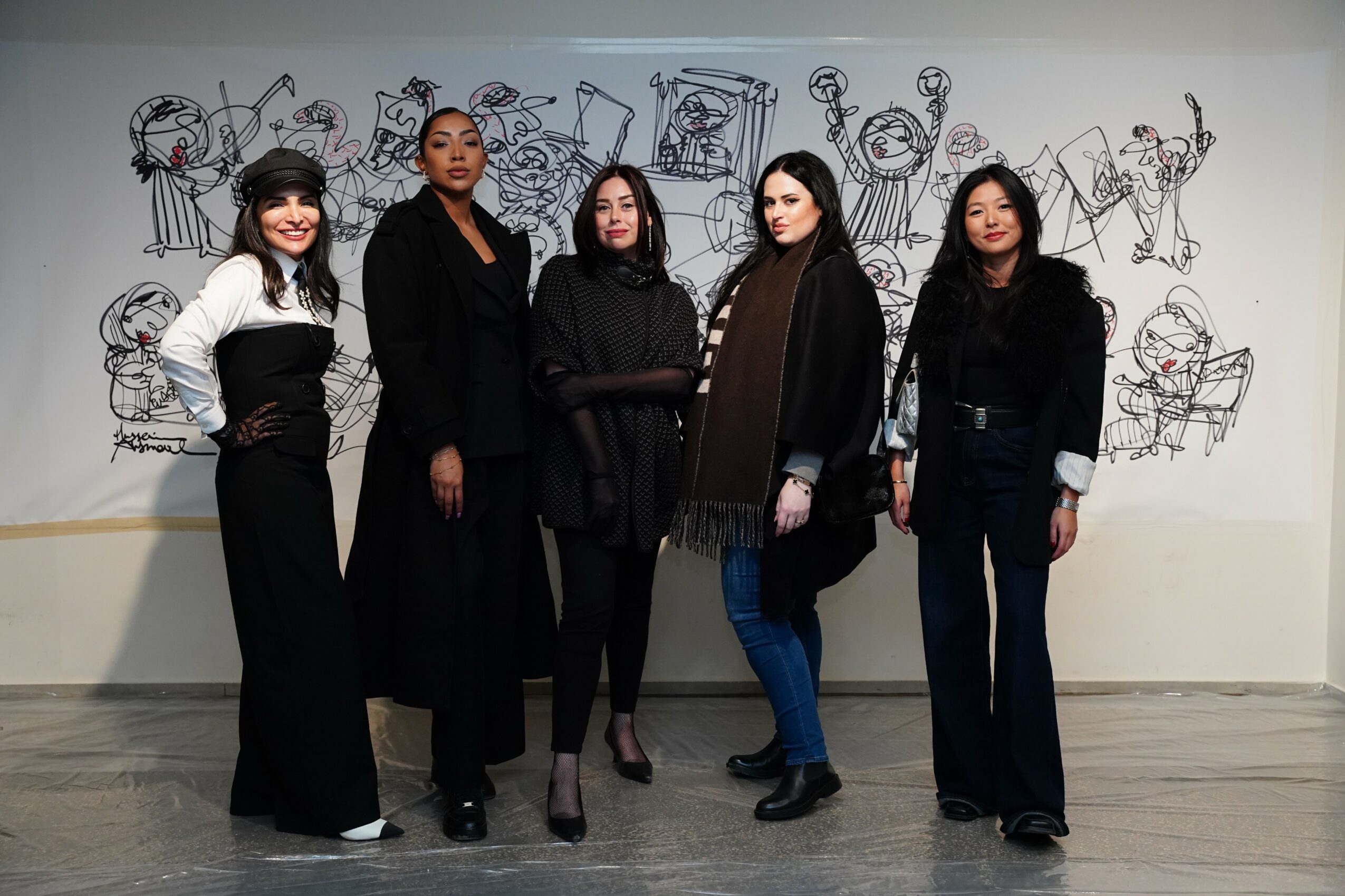 Five women stand in front of a wall with line drawings of people and objects, posing for a photo.