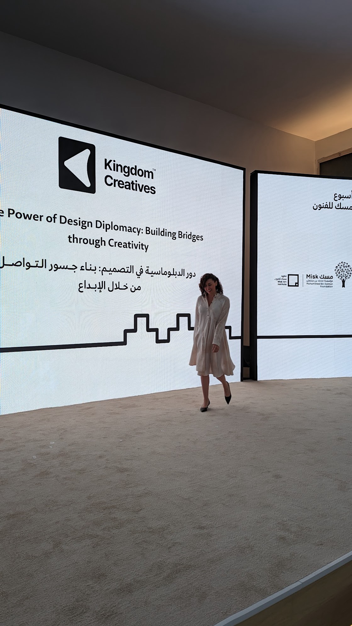 Person standing in front of large digital display with text and graphics, in an indoor setting.