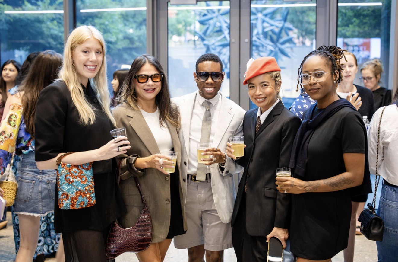 Group of five diverse people smiling and holding drinks at an indoor event, with large windows in the background.