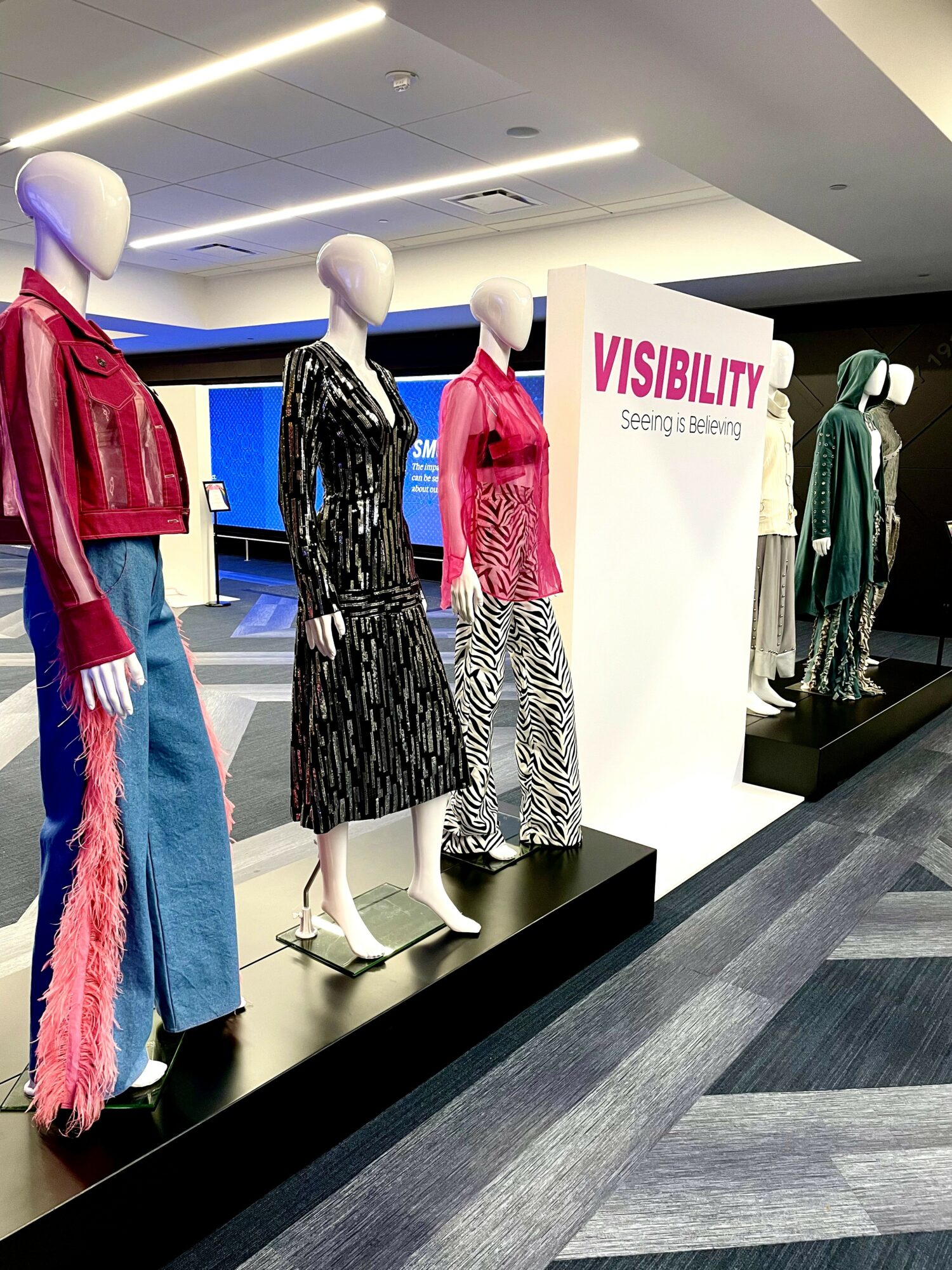 Four mannequins display colorful outfits in a store window, with a sign reading 'VISIBILITY' behind them.
