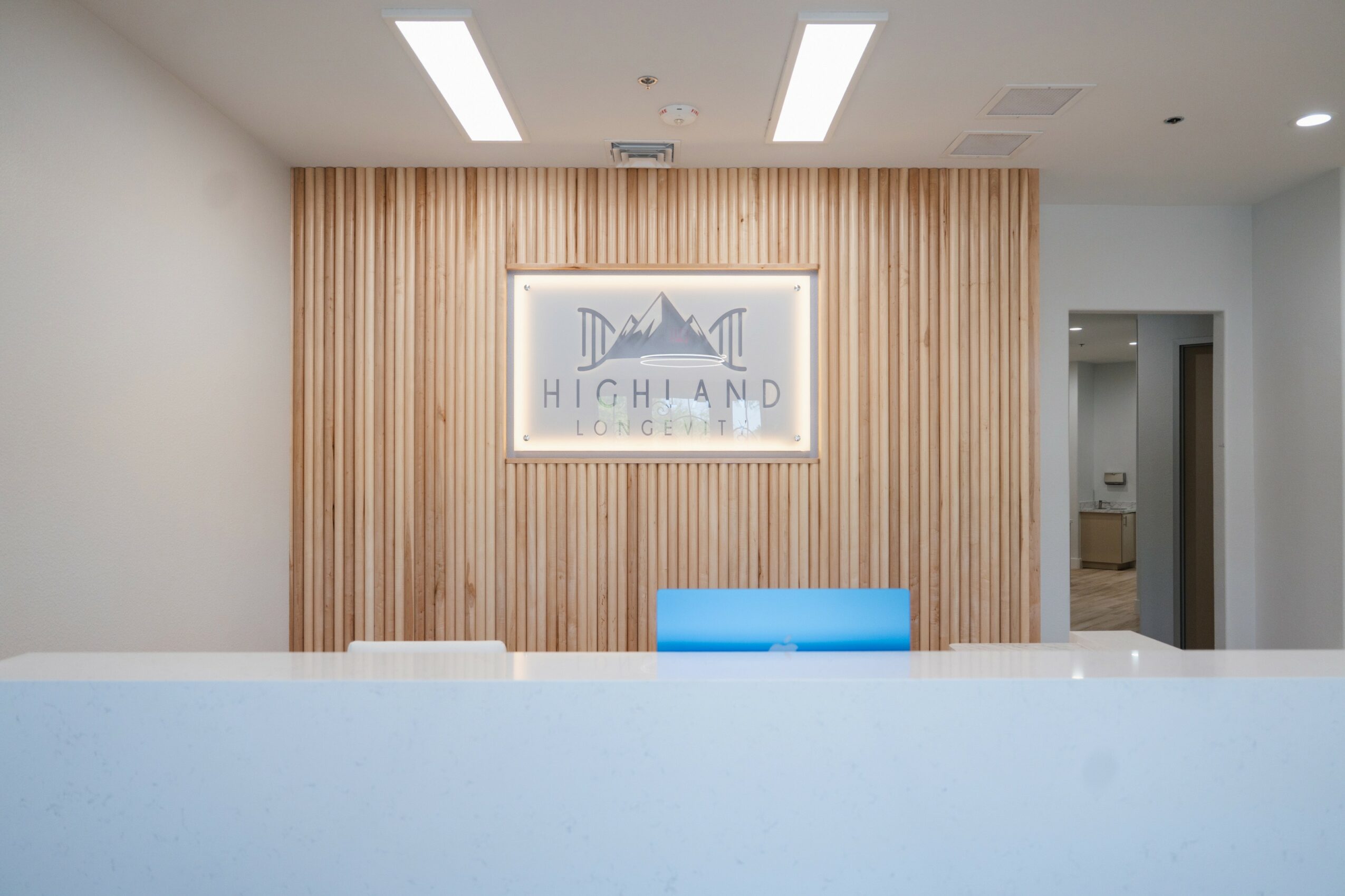 Reception area with a wooden wall, a framed sign, and a blue chair, with a white counter in the foreground.