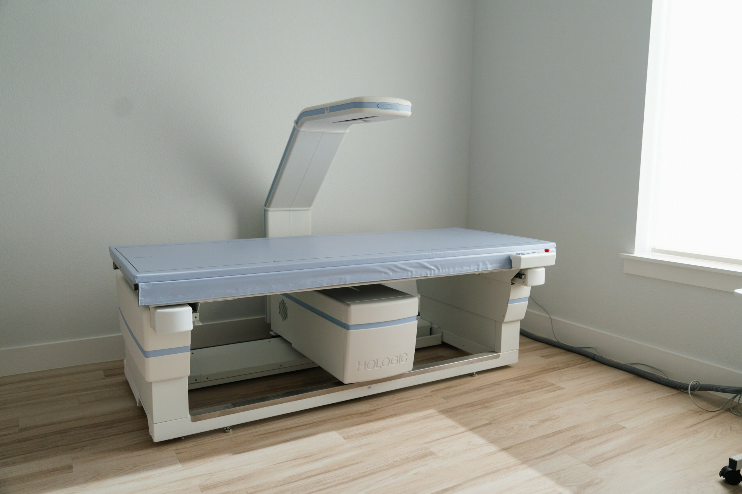 Medical examination table with an adjustable headrest in a room with wooden floor and window, no people present.