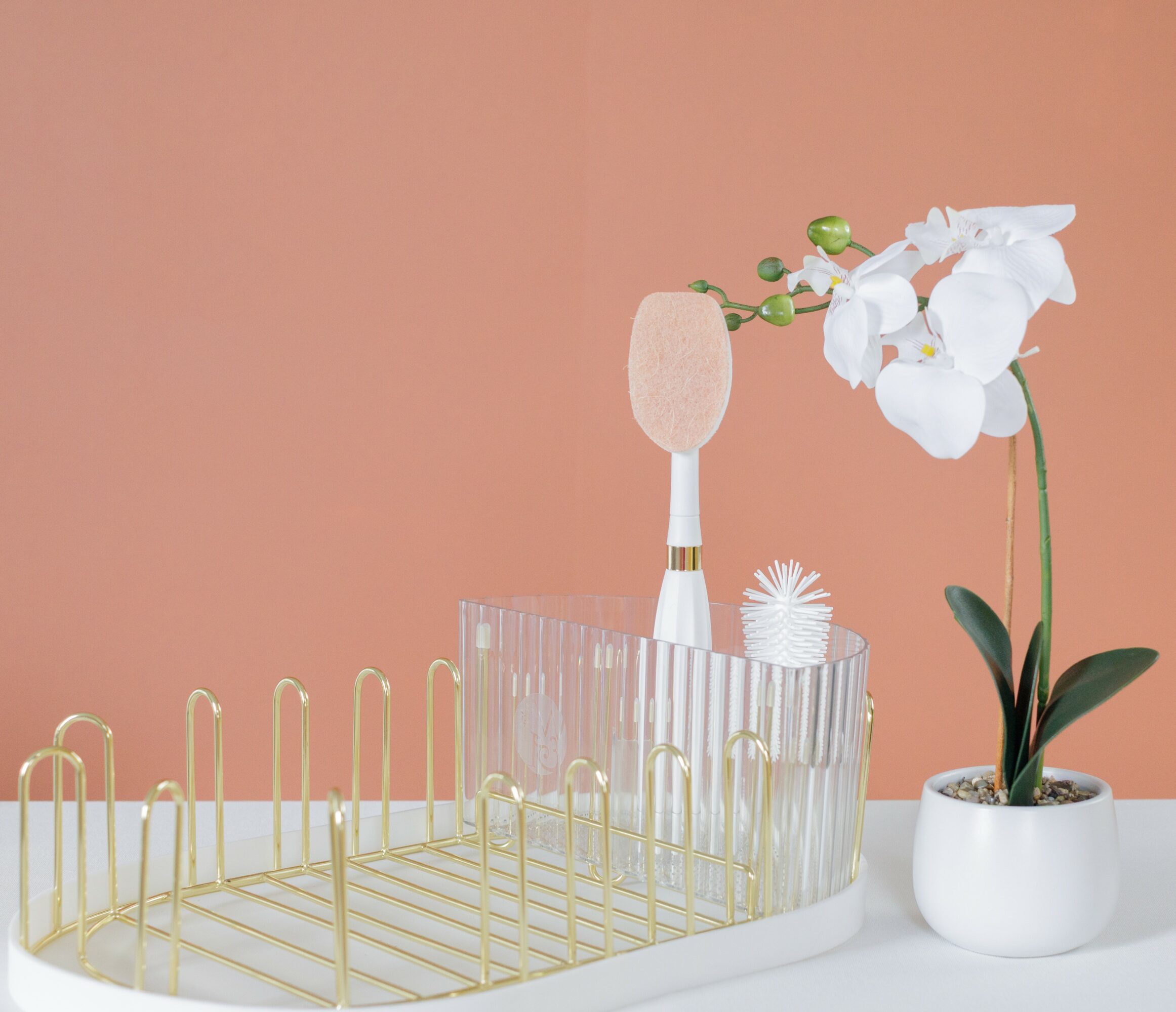 Toothbrush, white orchid in a white pot, and a decorative item on a white surface against a pink background.