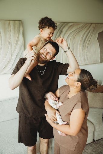 A man, woman, young child, and baby in a living room, smiling and interacting happily.