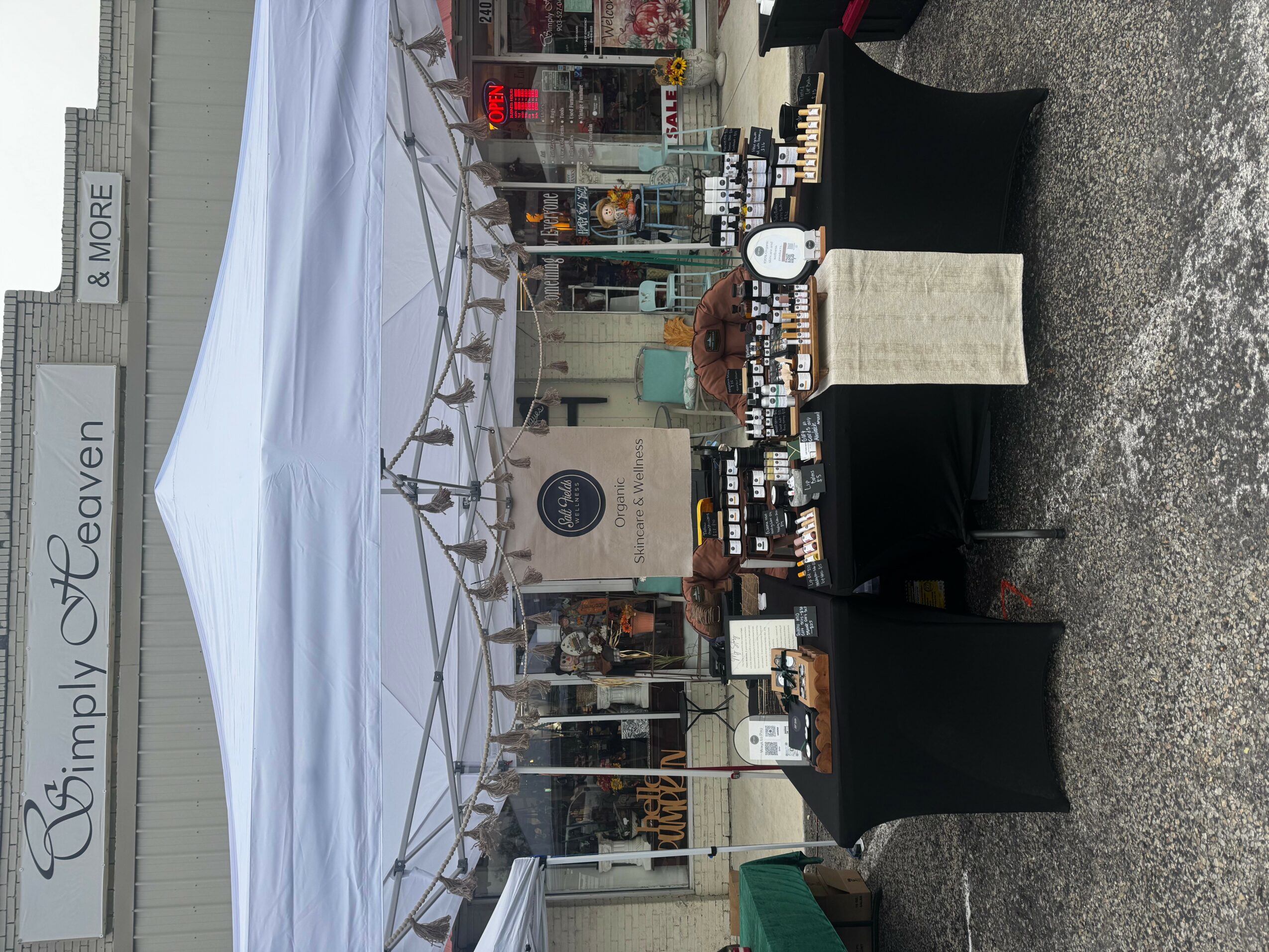 Outdoor market stall with various products on display, set up under a white canopy, with a sign reading 'Simply O'Ceaven' in the background.