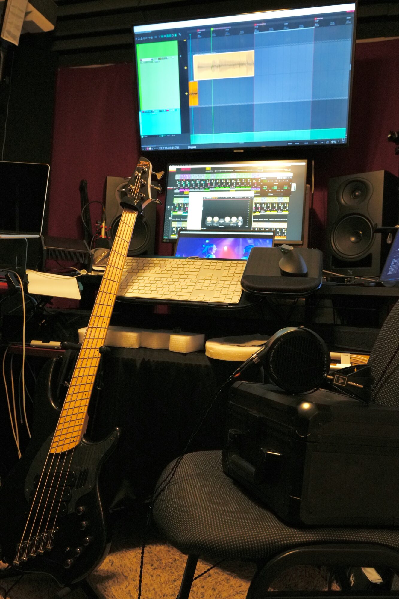 Music studio workspace with a guitar, computer monitors, audio equipment, and a chair.