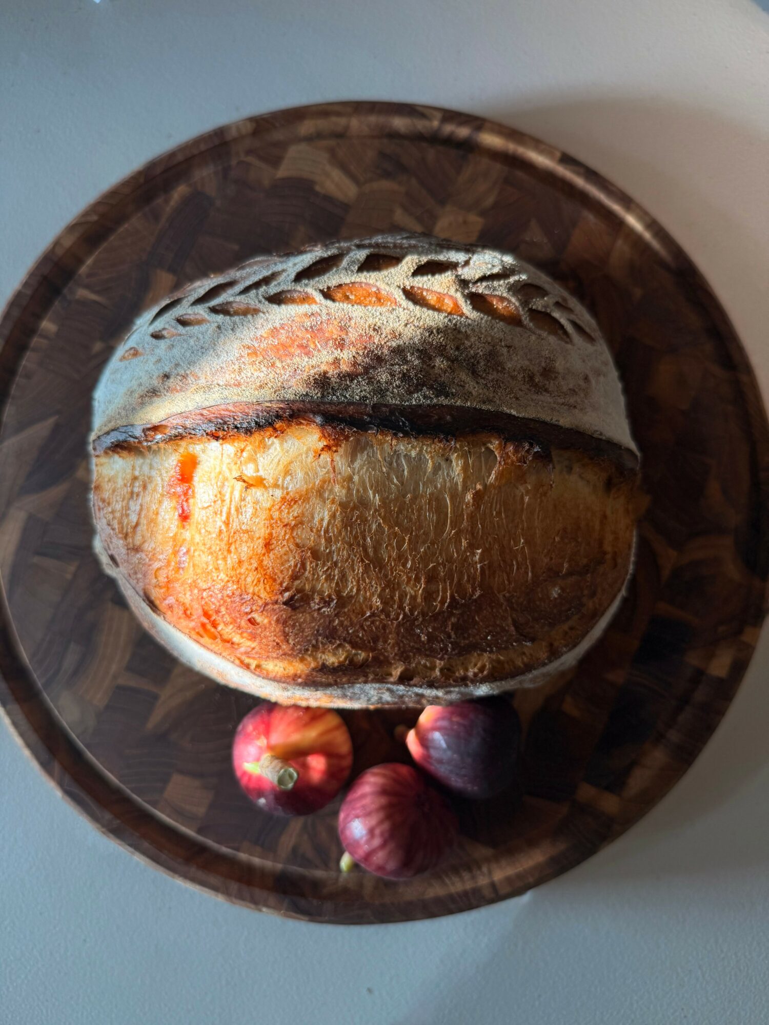 Loaf of bread on a dark wooden plate with three small red fruits, viewed from above.