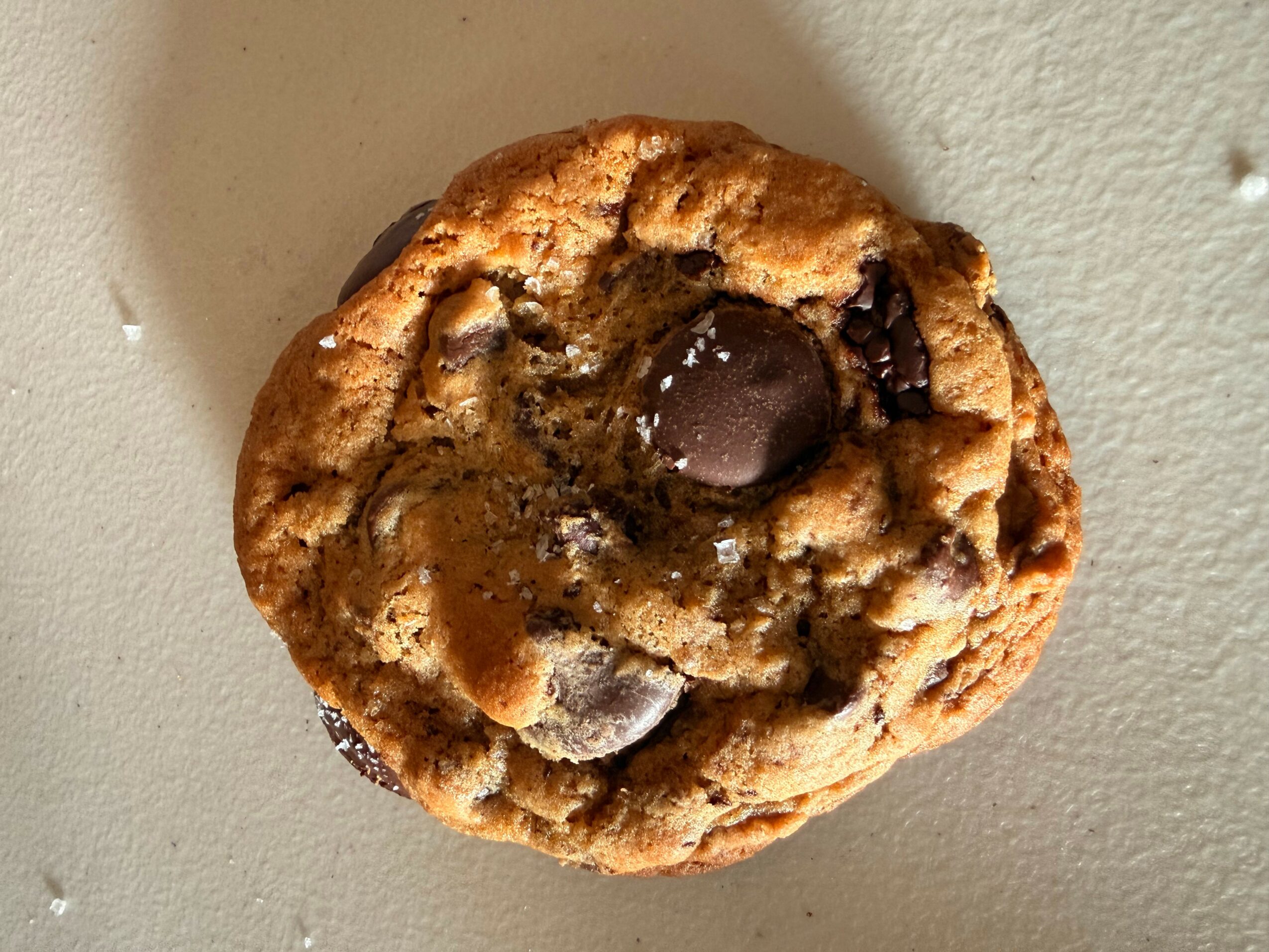 Chocolate chip cookie with melted chocolate chunks on a light-colored surface.
