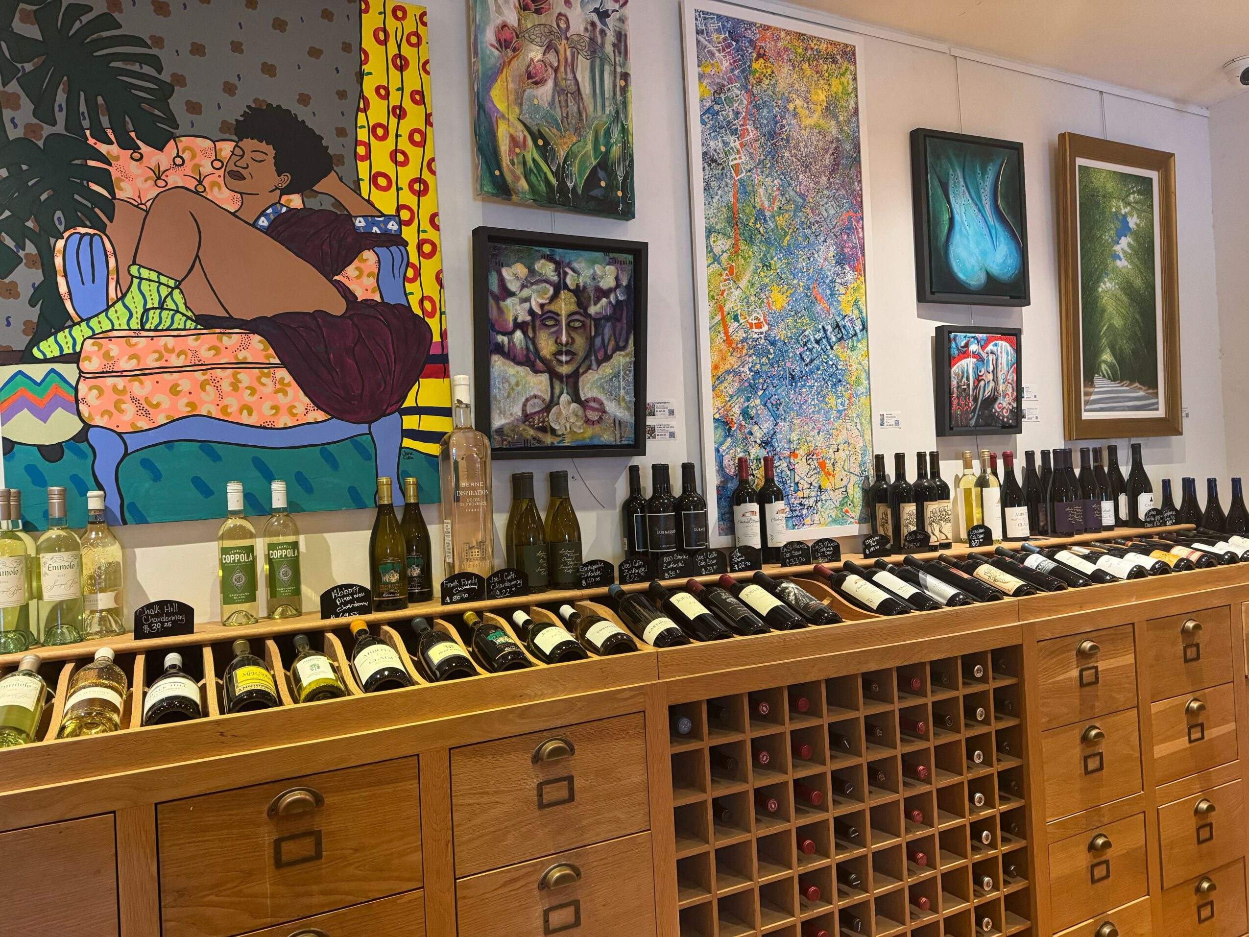 Gallery with paintings and colorful artwork on walls, wooden storage units above, and a person in the scene.