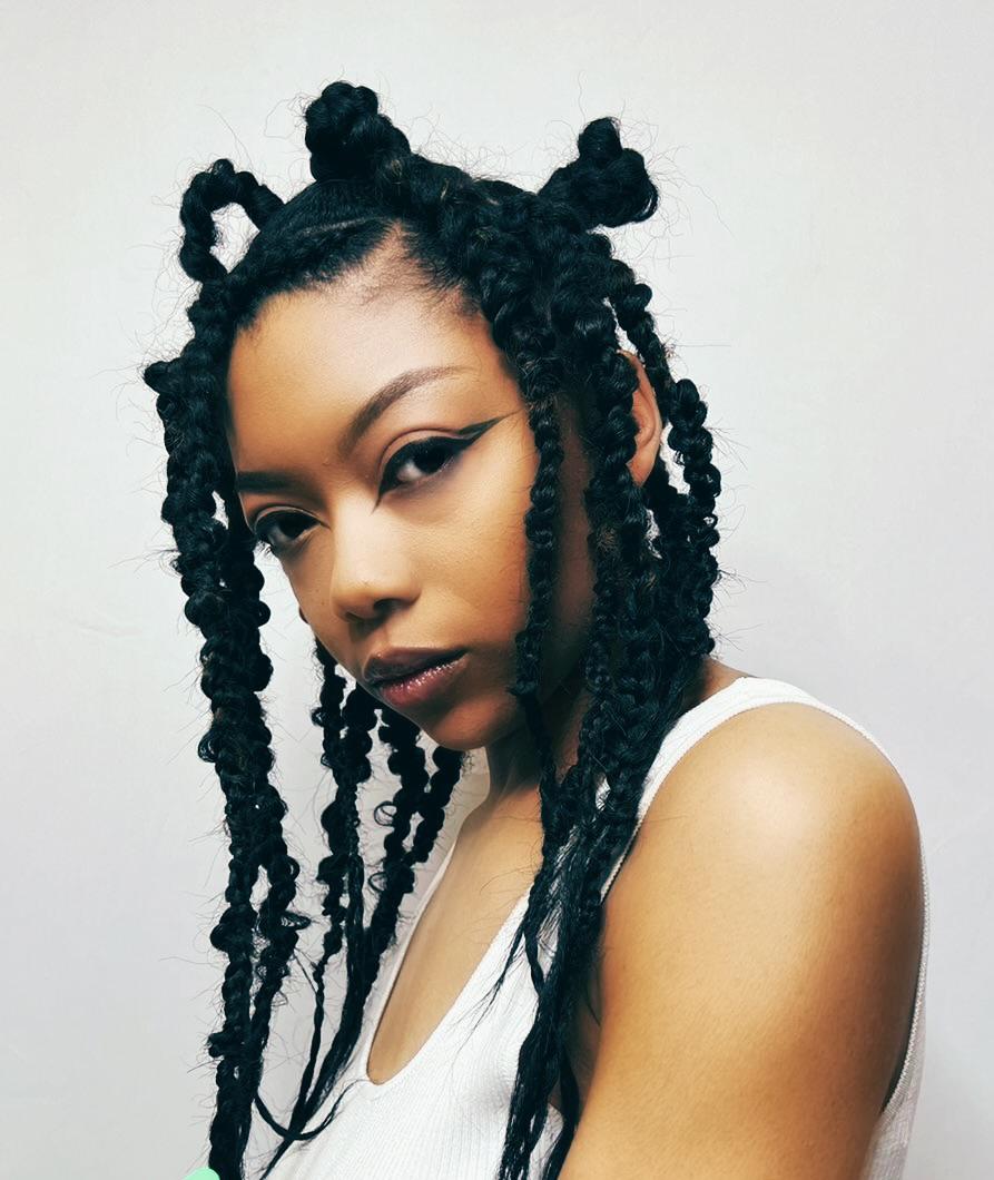 Portrait of a woman with styled hair and makeup, wearing a white top, against a plain background.
